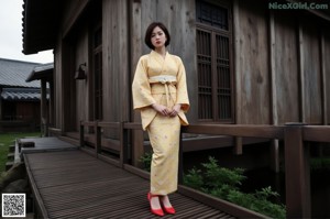 A woman in a yellow kimono standing on a wooden walkway.