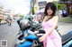 A woman in a pink dress standing next to a blue motorcycle.