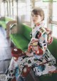 A woman in a kimono sitting on a green bench.