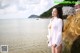 A woman in a white shirt standing on a rock by the water.