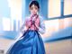 A woman in a blue and pink hanbok standing in front of a window.